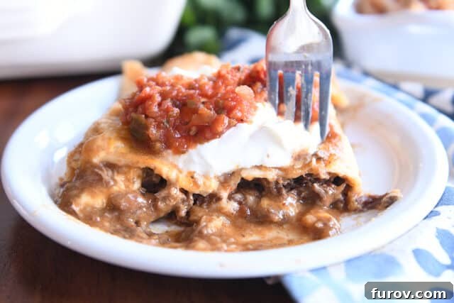 Two saucy enchiladas on a white plate with a fork, showcasing the rich red sauce and melted cheese.