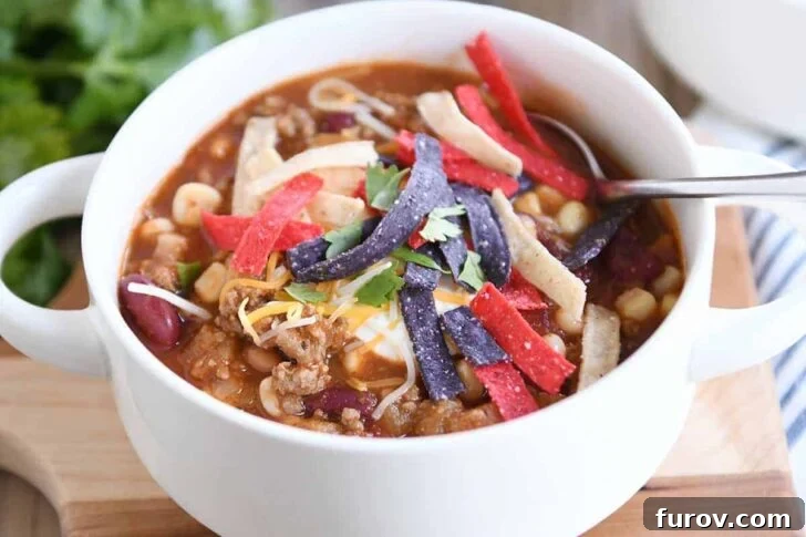 White bowl filled with taco soup, generously topped with cheese, sour cream, and crispy tortilla strips.