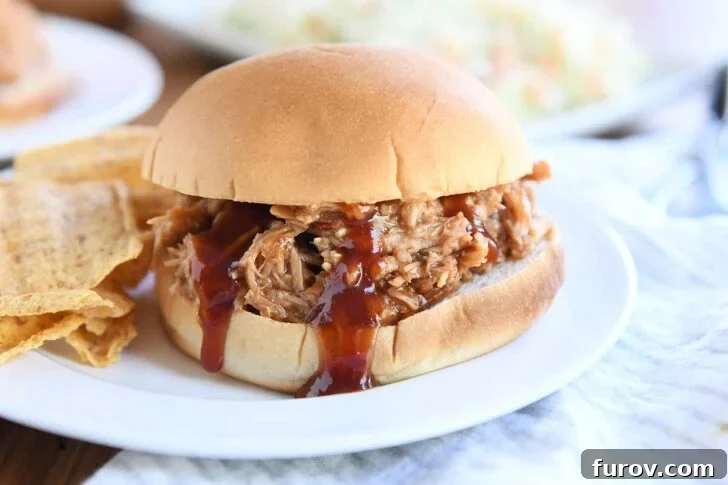 BBQ pork sandwich on bun on white plate with coleslaw and pickles