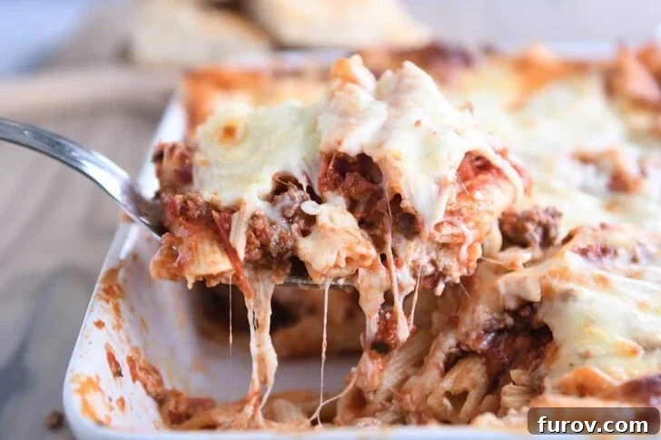 scooping a serving of easy cheesy weeknight pasta bake out of a white 9X13-inch pan, showcasing the golden-brown top and melted cheese