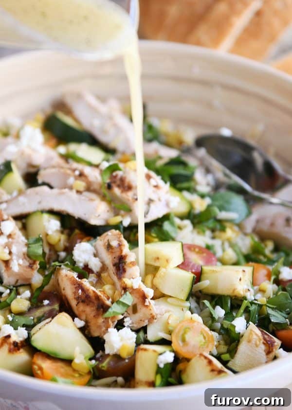 Close-up shot of zesty honey lime dressing being drizzled over a fresh grilled chicken orzo salad.