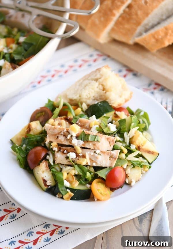 Plated serving of grilled orzo salad on double stacked white plates, accompanied by rustic crusty bread.
