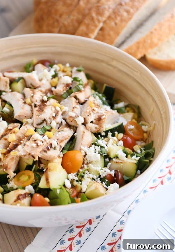A large white serving bowl filled with colorful grilled chicken orzo salad, ready to be served.