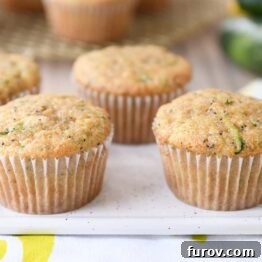 A cluster of golden-brown lemon poppy seed zucchini muffins on a white plate.