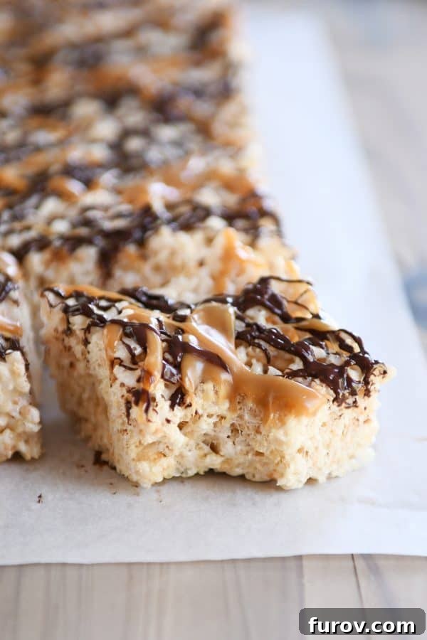 Toasted Coconut Caramel Crunch Bars 5 Bite taken out of Toasted Coconut Caramel Rice Krispie Treats on parchment paper.