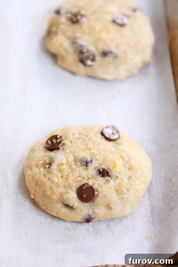 Pillowy Banana Bread Cookies 5 Two freshly baked banana bread cookies on a parchment-lined baking sheet, golden and inviting.