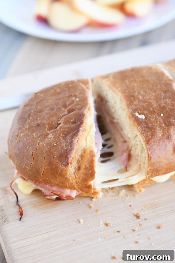 A perfectly golden ham and cheese sheet pan panini being cut into slices on a wooden cutting board, ready to serve.