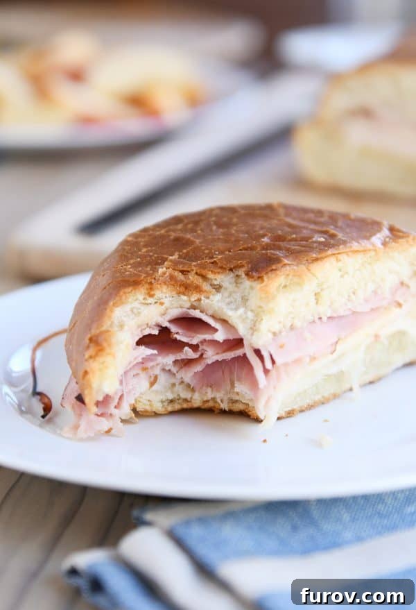 A close-up shot of a delicious ham and cheese sheet pan panini with a bite taken out, showing the melted cheese and toasted bread.