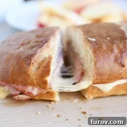 A slice of ham and cheese sheet pan panini on a wooden cutting board, ready for serving.