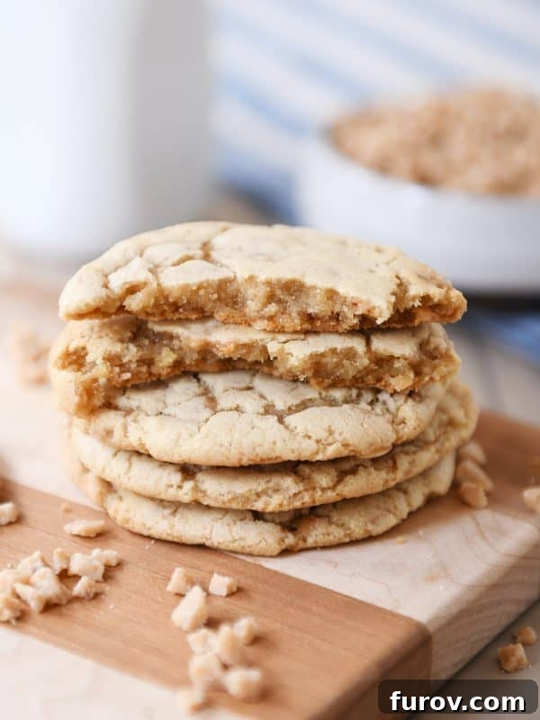A stack of thin and chewy toffee cookies on a wooden cutting board with one cookie broken in half, revealing its soft interior.