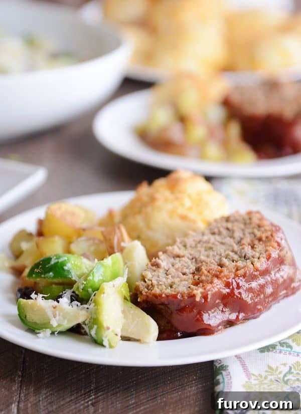 A slice of the best glazed meatloaf on a plate with vegetables and a biscuit.