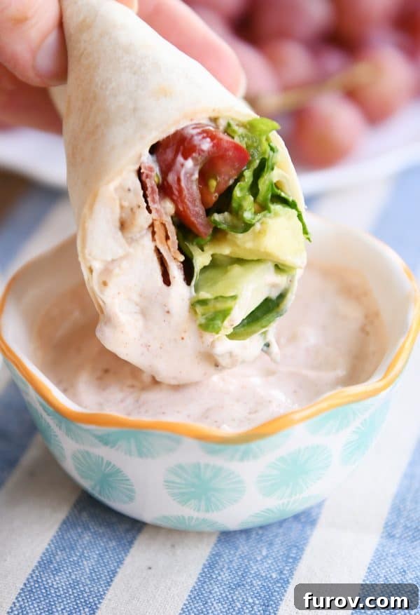 Craveable Chicken BLT Burritos with Creamy Southwest Dip 3 Close-up shot of a hand dipping a Chicken BLT Burrito into a creamy Southwest dipping sauce, highlighting the rich texture of the sauce and the appetizing burrito.