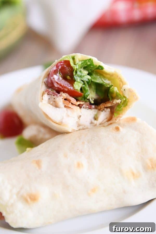 Craveable Chicken BLT Burritos with Creamy Southwest Dip 4 A Chicken BLT Burrito with a bite taken out, revealing the vibrant layers of chicken, bacon, lettuce, tomato, and avocado, resting on a white plate.