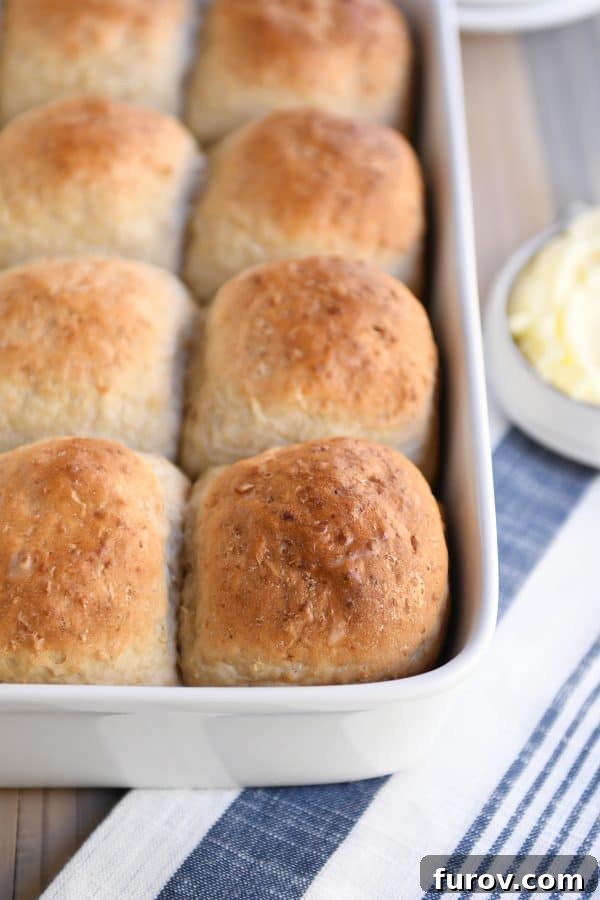 Fluffy honey oat dinner roll sitting on top of pan filled with rolls.