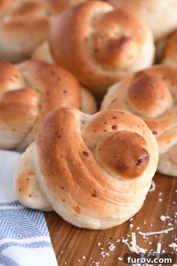 Simple Parmesan Garlic Knots 11 Several golden brown, baked Parmesan breadstick knots beautifully arranged on a rustic wooden board, accompanied by a white and blue patterned cloth.