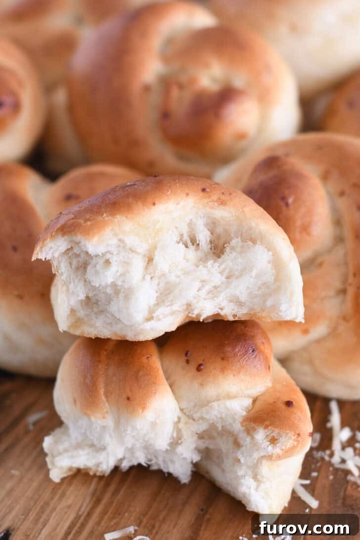 Simple Parmesan Garlic Knots 12 A Parmesan breadstick knot torn into two halves, stacked artfully on top of each other, showcasing its soft, fluffy interior texture.