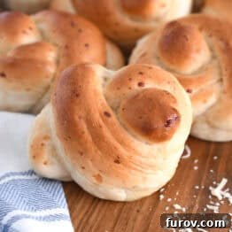 Simple Parmesan Garlic Knots 13 Several baked Parmesan breadstick knots arranged on a rustic wooden board with a white and blue patterned cloth beside them.