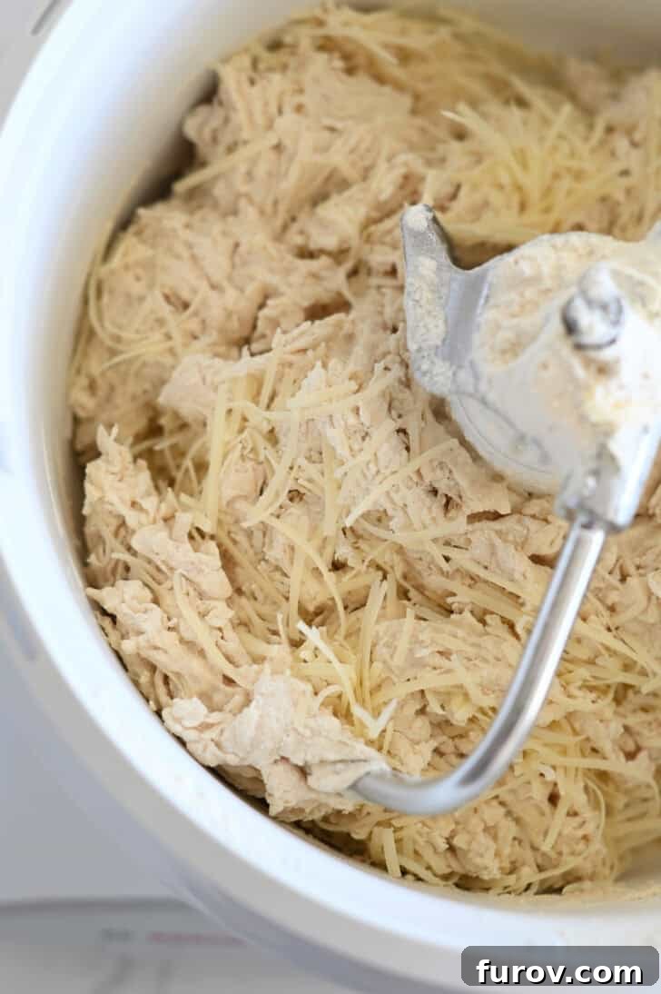 Simple Parmesan Garlic Knots 3 Freshly grated Parmesan cheese being added to the breadstick dough within a white Bosch mixer bowl, accompanied by a dough hook.