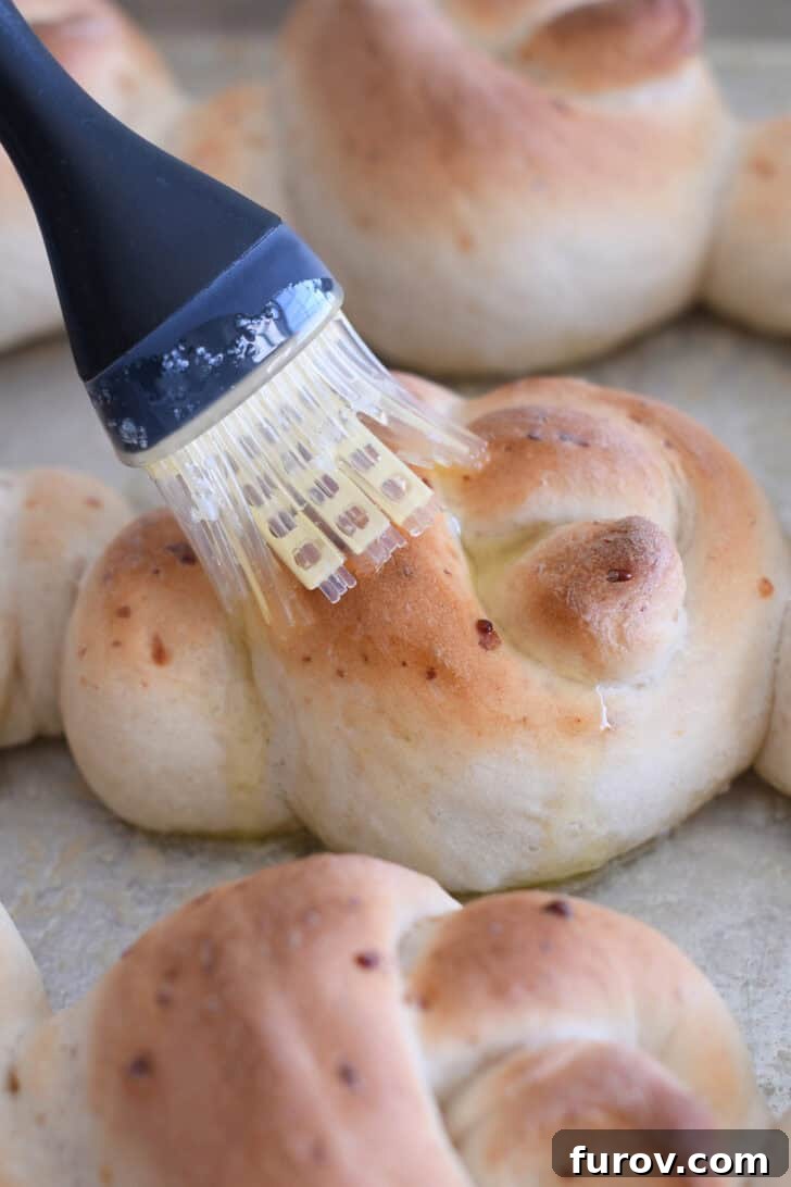 Simple Parmesan Garlic Knots 6 A culinary brush generously applying melted butter over the top of a hot, freshly baked Parmesan breadstick knot, fresh out of the oven.