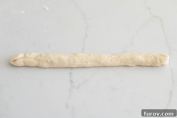 Simple Parmesan Garlic Knots 7 A section of breadstick dough expertly rolled into a long, thin, uniform strip, ready for shaping on a clean white countertop.