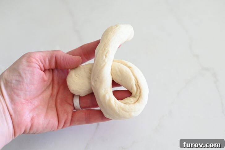 Simple Parmesan Garlic Knots 8 The process of forming a breadstick knot, showing one end of the dough strip being twisted over the other to create a loop.