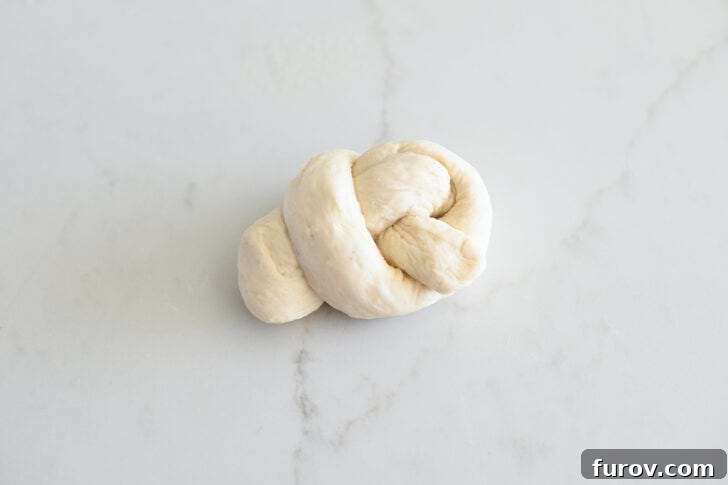 Simple Parmesan Garlic Knots 10 A perfectly formed breadstick dough knot resting on a clean white countertop, showcasing the elegant and classic shape achieved.