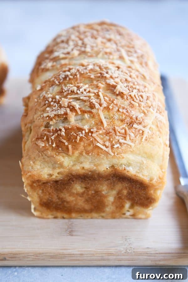 A golden-brown loaf of Parmesan Bagel Bread, perfectly sliced and resting on a rustic wooden cutting board.