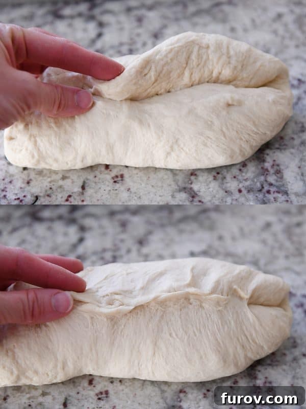 Raw bread dough being carefully rolled and patted into a uniform loaf shape on a clean surface after being folded and sealed.