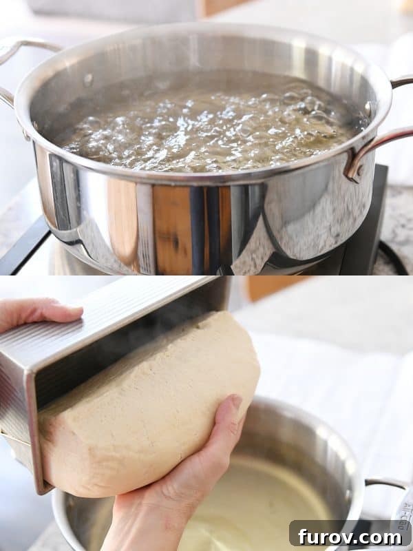 A large pot of water boiling vigorously on the stove, with a loaf of bagel bread dough poised to be carefully placed in the hot water.