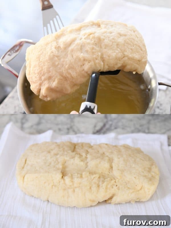 A spatula carefully lifting a boiled loaf of bagel bread out of the pot of water and onto a towel, ready for the next step.