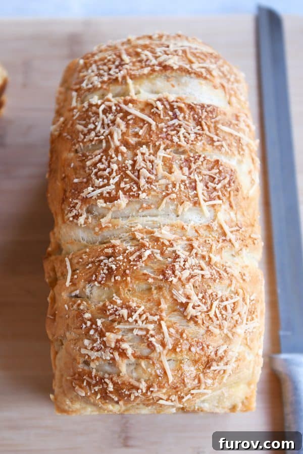 A top-down view of a golden-crusted Parmesan Bagel Bread loaf on a wooden cutting board, invitingly sliced and ready for serving.