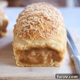 Loaf of parmesan bagel bread on wood cutting board.