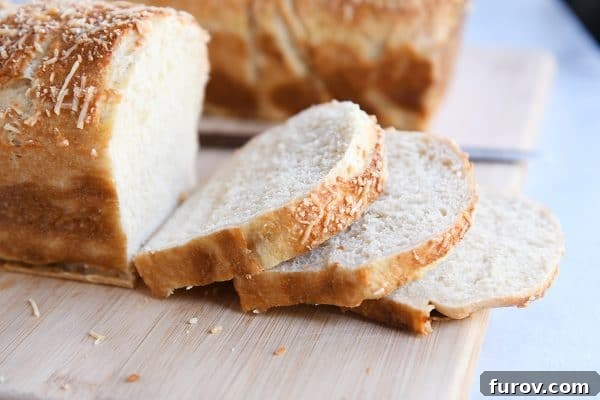 A freshly baked loaf of Parmesan Bagel Bread on a cutting board, with several slices already cut, revealing the cheesy, airy interior.