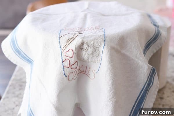 A bowl of bread dough, covered with a beautiful hand-embroidered kitchen towel, resting and slowly rising in a warm environment.