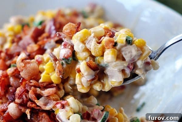 A spoon scooping a generous bite of creamy corn topped with crispy bacon pieces, highlighting its rich texture.