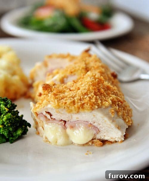 Chicken cordon bleu cut open on a white plate, showing the melted ham and cheese inside.