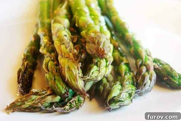 Roasted asparagus on a white plate, garnished with fresh herbs and a slice of lemon.