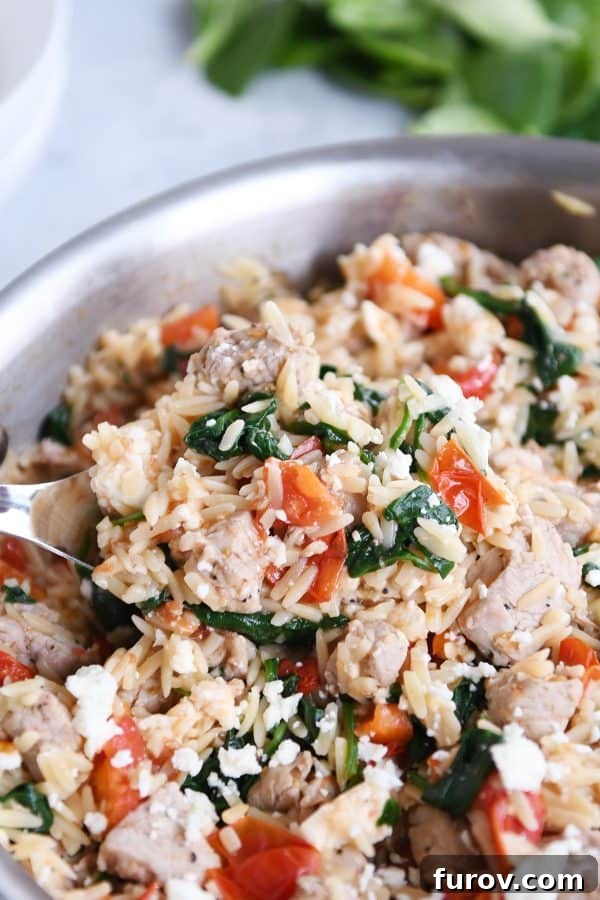 Mediterranean orzo skillet with serving spoon, ready to be served.