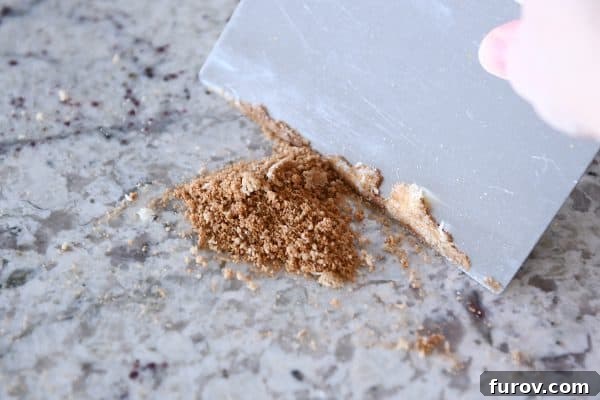 Master Cheryl's Famous Cinnamon Rolls: A Step-by-Step Guide to the Best Recipe and Baking Secrets 29 A bench scraper being used to efficiently clean flour and dough residue from a kitchen counter, demonstrating its usefulness.