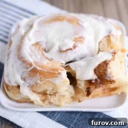 Master Cheryl's Famous Cinnamon Rolls: A Step-by-Step Guide to the Best Recipe and Baking Secrets 31 A single, perfectly frosted cinnamon roll, showcasing its delicate swirls and plush texture, sits on a white square plate.