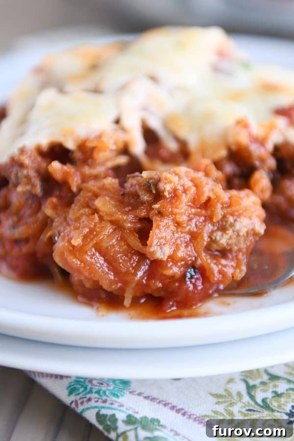 Close up of a forkful of spaghetti squash spaghetti bake topped with cheese on a white plate.