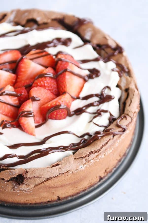 Deep Dark Chocolate Slump 3 Decadent fallen chocolate cake garnished generously with creamy whipped cream, vibrant fresh strawberries, and a glossy chocolate drizzle, presented on a white plate.
