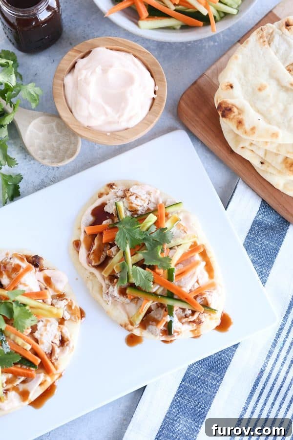 Fast Chicken Banh Mi Flatbread with Two Amazing Sauces 3 Top down view of Chicken banh mi flatbread with pickled cucumbers and carrots on white platter, highlighting the fresh toppings.