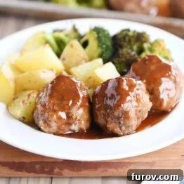 A white plate filled with meatballs drizzled in sweet and sour sauce and roasted vegetables.