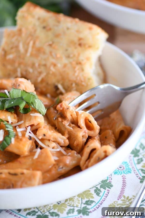 Ultimate Instant Pot Creamy Faux-Baked Ziti 2 A generous serving of creamy Instant Pot baked ziti with fresh basil and a piece of focaccia bread on a white plate, ready to be enjoyed.