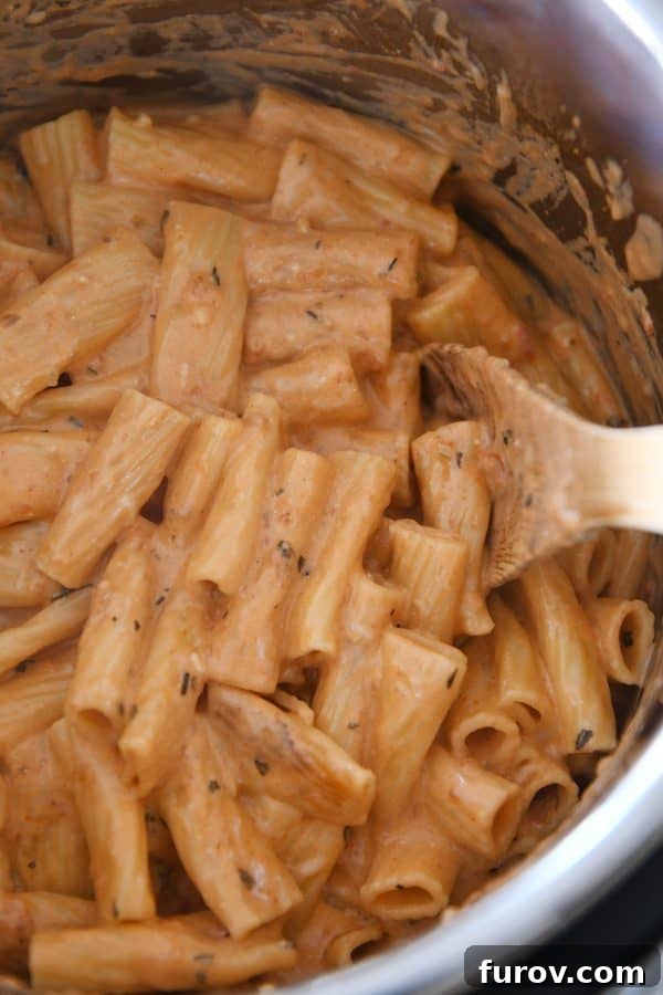 Ultimate Instant Pot Creamy Faux-Baked Ziti 5 A person stirring the creamy Instant Pot baked ziti in the inner pot with a metal spoon after cooking, showing the rich texture of the sauce and pasta.