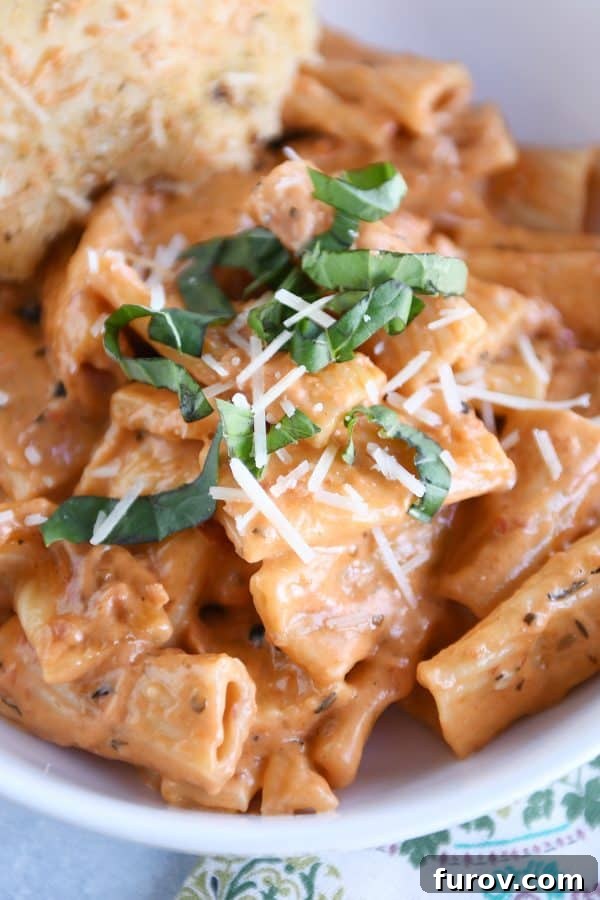 Ultimate Instant Pot Creamy Faux-Baked Ziti 6 A close-up view of creamy Instant Pot baked ziti in a white bowl, garnished with fresh basil leaves and a sprinkle of Parmesan cheese, highlighting its rich texture.