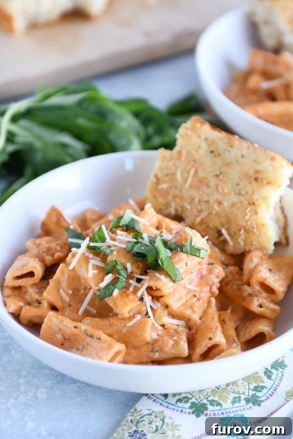 Ultimate Instant Pot Creamy Faux-Baked Ziti 7 A white bowl filled with creamy Instant Pot baked ziti, served alongside a slice of golden focaccia bread, showcasing a comforting and complete meal.