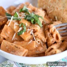 Ultimate Instant Pot Creamy Faux-Baked Ziti 8 A close-up shot of a white bowl filled with rich, creamy Instant Pot baked ziti, garnished with fresh basil, accompanied by a piece of focaccia bread.
