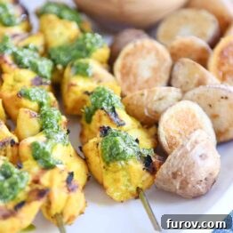 Close up view of green sauce on Moroccan chicken skewer with a couple roasted potatoes.